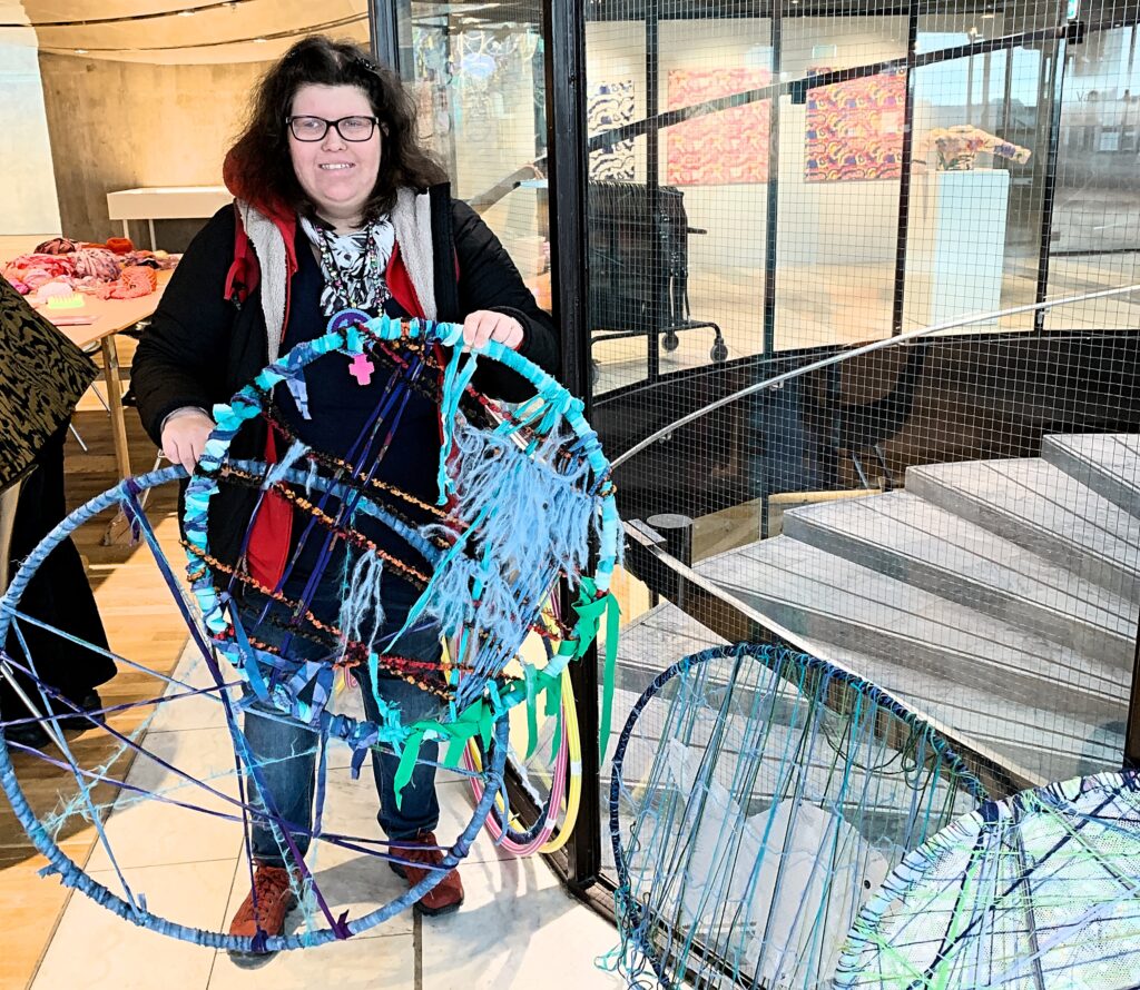 Hanna står med två tingar i händerna och hittar in i kameran med ett leende.